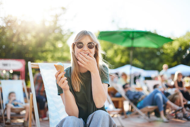 美味吃冰淇淋的女士在笑阳光明媚的日子里坐在公园里吃冰淇淋的年轻女性的画像零食举行冰