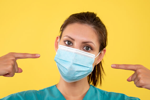 护士正面近距离观察黄色背景上戴着无菌口罩的女医生女医生前面肖像