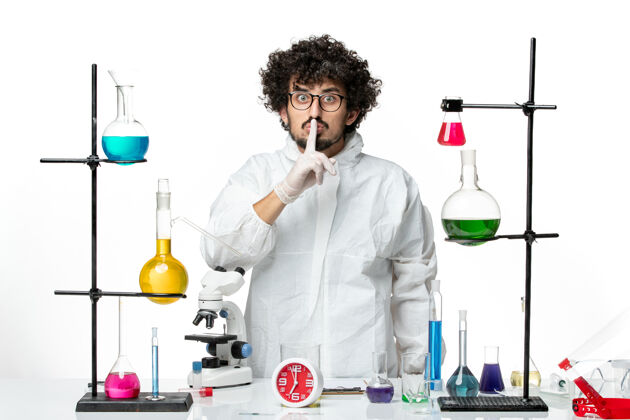 实验室外套正面图身着特殊套装的年轻男性科学家站在桌子旁 在白色的墙上拿着解决方案景观医院立场