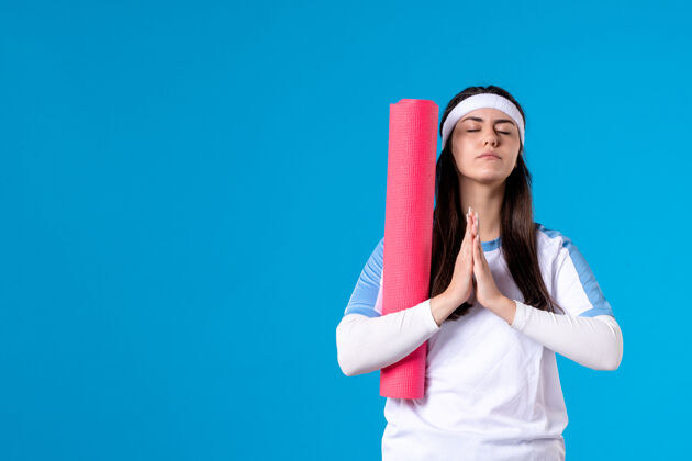 微笑前视图年轻女性 蓝色墙壁上有瑜伽垫制服身体年轻女性