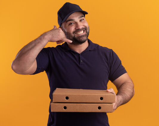 手势微笑的中年送货员身着制服 戴着帽子 手里拿着披萨盒 黄色的墙上孤立着显示打电话的手势帽子制服微笑