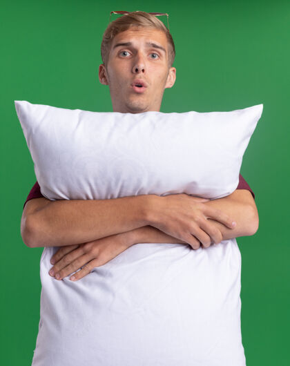 穿穿着红衬衫的年轻帅哥惊讶地抱住了隔离在绿墙上的枕头枕头衬衫惊喜