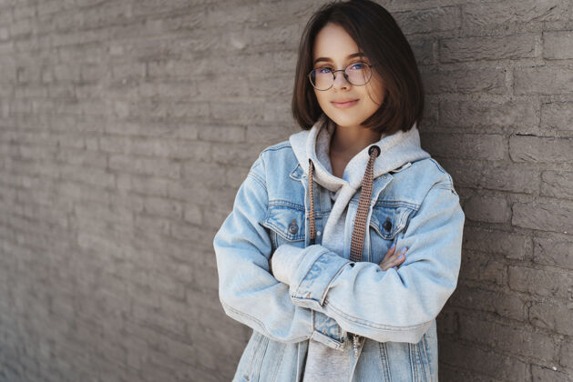 人漂亮的小女孩 短发 戴着眼镜 穿着街头风格的衣服 靠在砖墙上表情女孩微笑