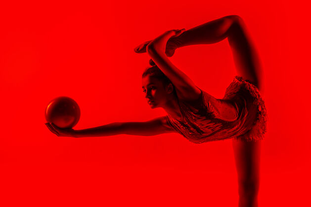 闪光年轻柔韧的女体操运动员被隔离在红色优雅韵律杂技