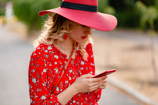 女性迷人的时尚金发微笑的女人在稻草红帽子和衬衫夏季时尚套装使用手机华丽时尚脸