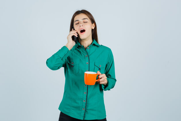 模特年轻的女士手里拿着一杯桔黄色的茶 穿着衬衫在讲手机 看起来很困倦 眼前一亮手机茶电话