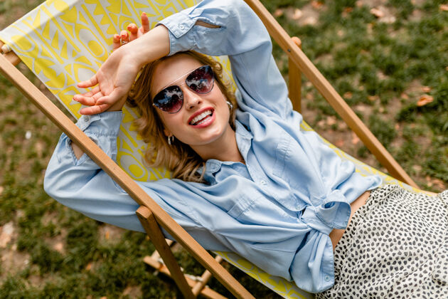 春天迷人的金发微笑的女人 穿着时髦的服装 轻松地坐在躺椅上头发夏天快乐