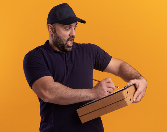 帽子一个穿着制服 戴着帽子的中年送货员吓了一跳 在黄色墙上的比萨饼盒的剪贴板上写着什么男人剪贴板害怕