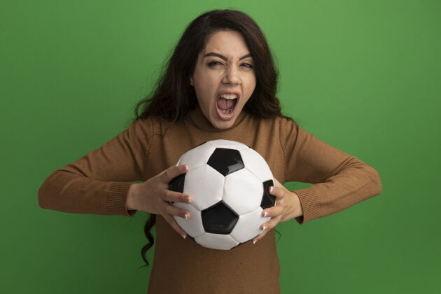 年轻愤怒的看着镜头年轻漂亮的女孩拿着球孤立在绿色的墙上女孩坚持愤怒