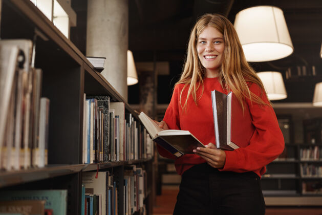 摊位红发女孩 学生站在书架旁的图书馆里 一边看书一边微笑教科书年轻研究