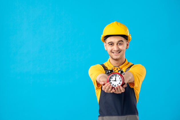 工人身着黄色制服 蓝色墙上挂着时钟的快乐男工人的正面图帽子迟到人