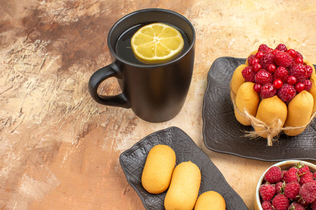 茶一个礼品蛋糕和茶在一个黑色的杯子与柠檬和饼干上的混合颜色表近距离观察果汁水果早餐