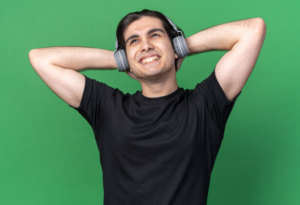 T恤穿着黑色t恤 戴着耳机 手放在脖子上的年轻帅哥 在绿色的墙上与世隔绝年轻人小伙子放松
