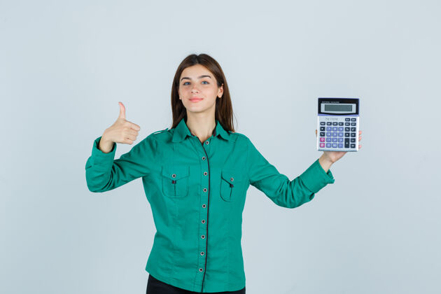积极拿着计算器的年轻女士 穿着绿色衬衫 大拇指朝上 看上去很高兴正视图夏天衬衫前面