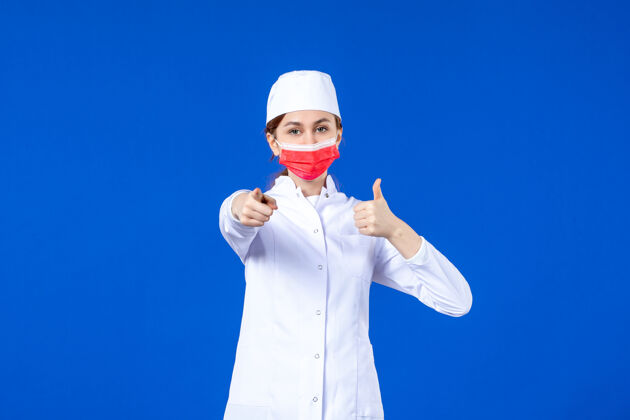 套装正面图身着医疗服的年轻护士 蓝色墙上戴着红色防护面具红色年轻护士病毒