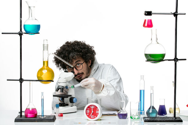烧杯正面图身着特殊套装的年轻男性科学家在白墙上打针科学医生实验室