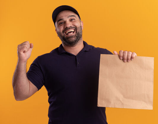 送货快乐的中年送货员穿着制服 戴着帽子 手里拿着一个纸食品包 在黄色的墙上显示“是”的手势是的手势男人