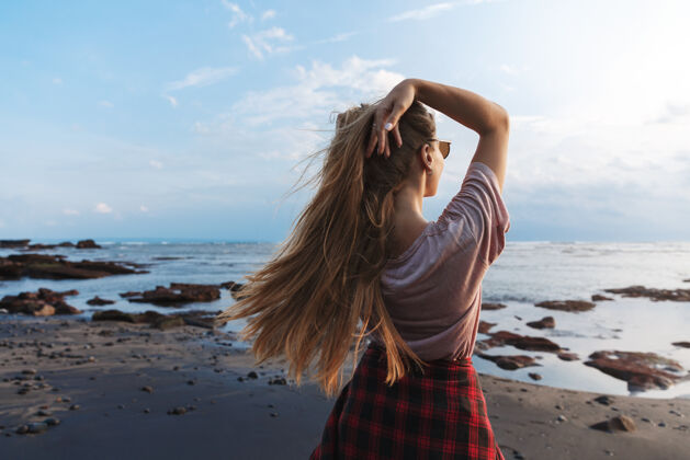 自然背面是一个留着长发的旅行女孩 站在黑色的火山沙滩上欣赏蓝色的海景比基尼泳装泻湖