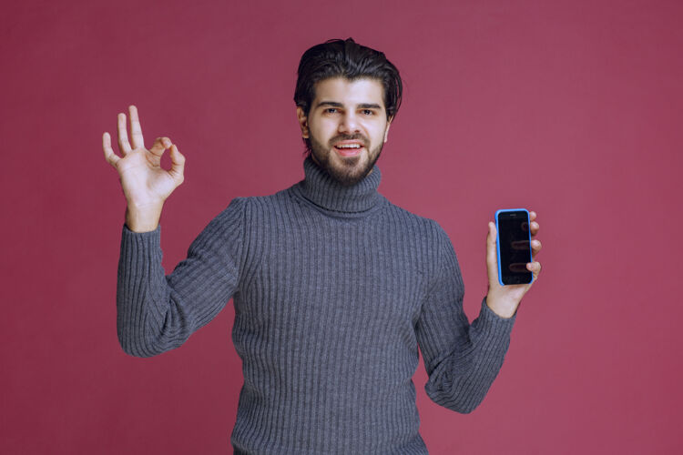 姿势拿着智能手机做手势的男人积极促销服装