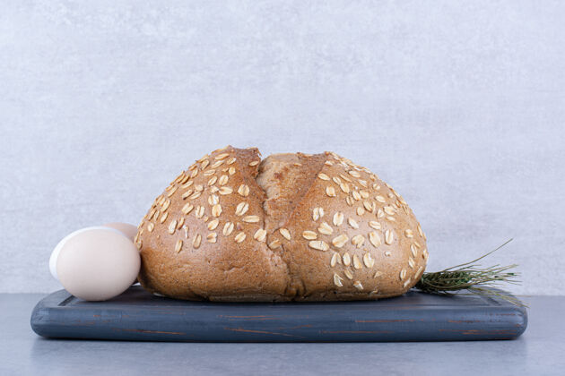 小麦一个鸡蛋 一条面包和一根麦秆放在大理石表面的木板上农产品烘焙食品薄片