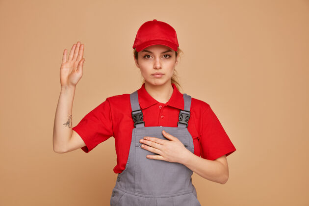 建筑严肃的年轻女建筑工人穿着制服 戴着帽子做承诺手势帽子承诺制服
