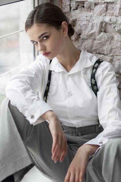 灰色背景优雅的女模特穿着优雅的白衬衫和吊带在橱窗里摆姿势全新的女性概念严肃女人吊带