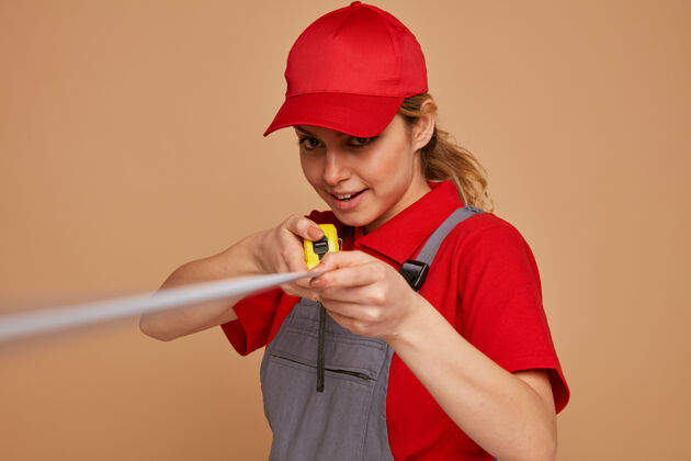 兴奋兴奋的年轻女建筑工人戴着帽子 穿着制服 向镜头伸出卷尺棕色工人胶带