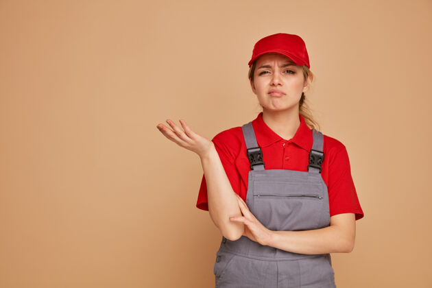 年轻笨手笨脚的年轻女建筑工人戴着帽子 穿着制服 手空空的不知所措制服穿
