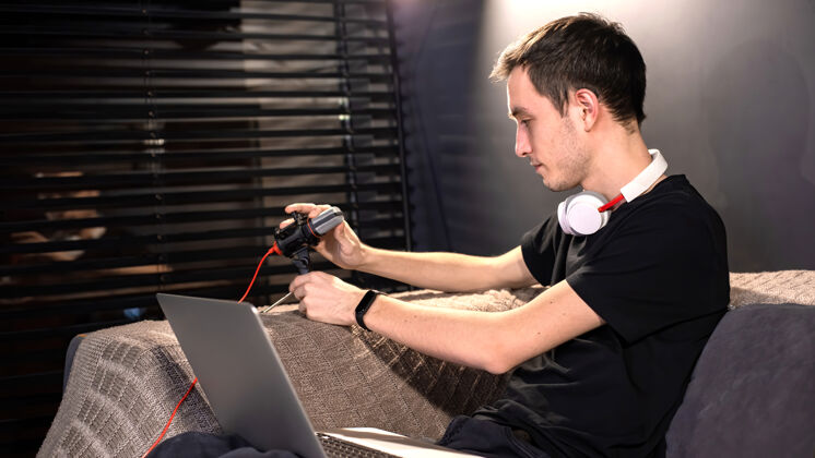 多媒体年轻的内容创作者正把麦克风 笔记本电脑放在膝盖上 坐在沙发上在家里工作电影自由职业者年轻