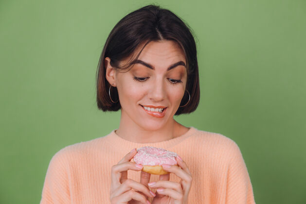 脸年轻时尚的女士穿着休闲的桃色毛衣 孤立地站在绿橄榄色的墙上 看着粉色的甜甜圈和饥肠辘辘的唇印空间肖像快乐饥饿