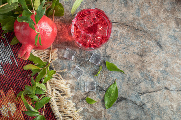 新鲜石榴和一杯果汁放在石头上 背景是叶子冰有机叶子