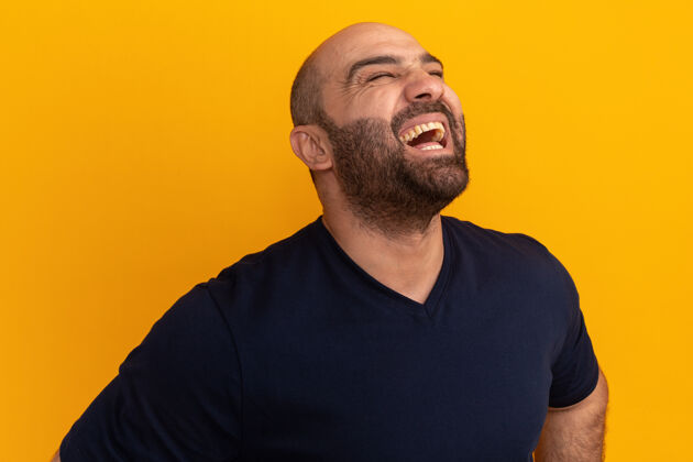 男人穿着海军t恤的胡须男人站在橘色的墙上笑出快乐和兴奋兴奋笑胡子