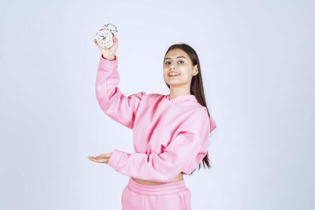 女人一个穿着粉色睡衣的女孩拿着一个闹钟 把它当作一个产品来推销营销方便人体模特