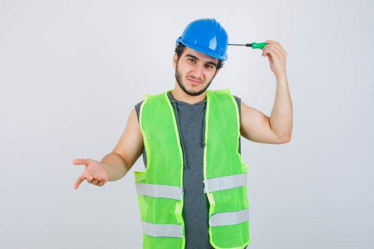 不知道年轻的建筑工人穿着制服 头上拿着螺丝刀头 犹豫不决地看着前方工人平面图头部