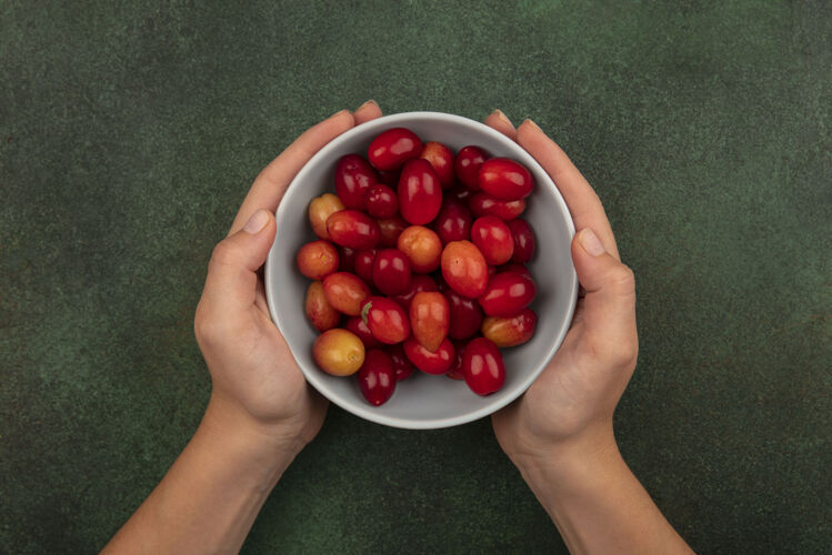 碗顶视图中的女性手拿着一碗新鲜的红凤梨樱桃在绿色的表面健康手营养