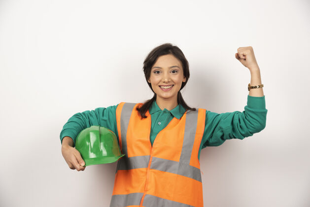 建筑微笑的女工程师展示肌肉 手持白色背景的头盔人女性工作