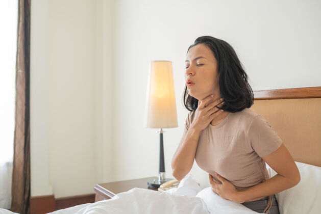 疼痛有咳嗽和喉咙感染的病妇躺在床上捂着脸咳嗽病毒不适症状