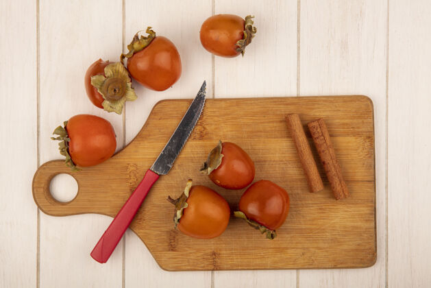 甜点俯视图软柿子在一个木制的厨房板与肉桂棒与刀在一个白色的木制表面棒肉桂刀