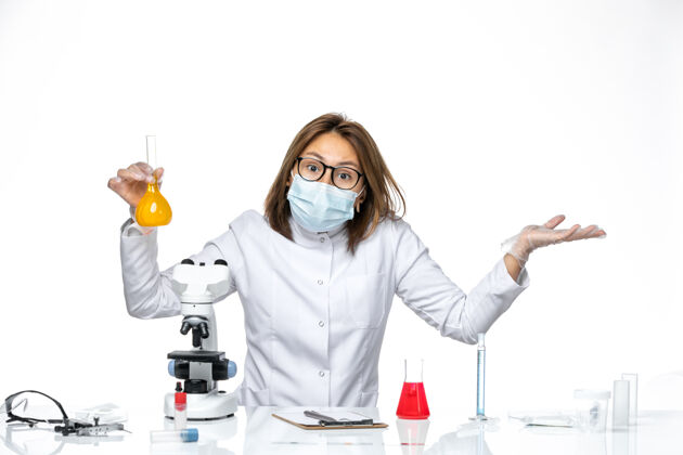 办公桌前视图白色医疗服和面具的女医生由于冠状病毒工作解决方案在白色办公桌上口罩病毒大流行