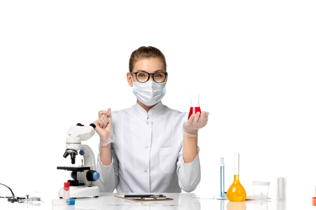 实验室外套正面图：女医生穿着医疗服 戴着面罩 因为科维德在白色办公桌上用溶液工作口罩病毒外套