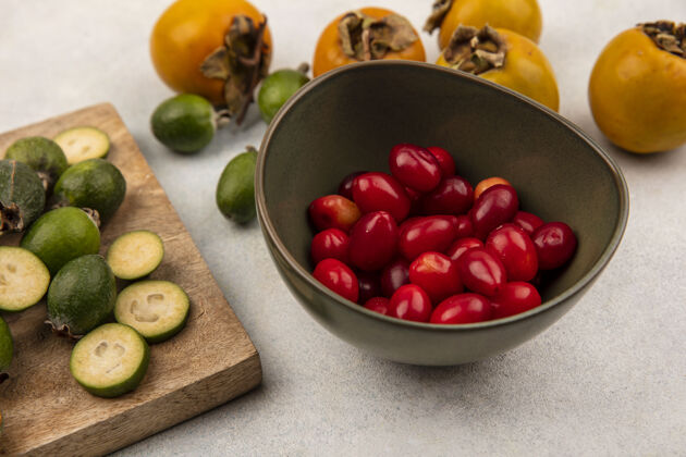 美味顶视图是一个碗上的山茱萸樱桃 上面有一个完整的和切成两半的新鲜果酱 隔离在一个木制的厨房板上 灰色的表面上有柿子配料肥肉板