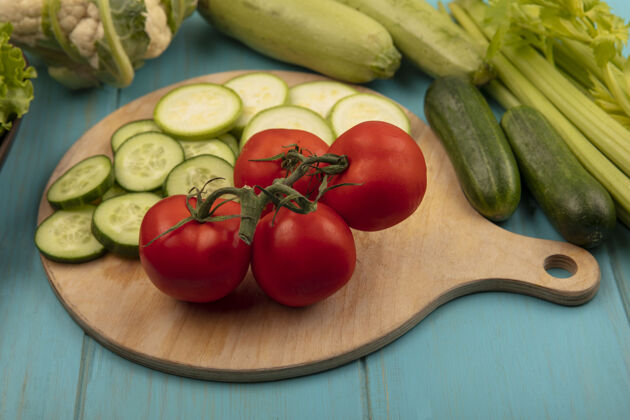 配料新鲜健康蔬菜的俯视图 如西红柿 切碎的黄瓜和西葫芦放在木制厨房板上 芹菜 菜花 黄瓜和西葫芦被隔离在蓝色的木制表面上板美味黄瓜