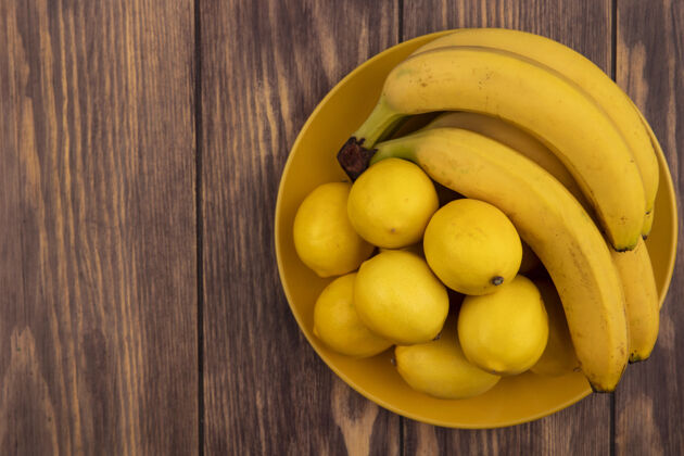 片黄色盘子上的黄皮柠檬顶视图 木制表面上有香蕉和复印空间皮营养美味