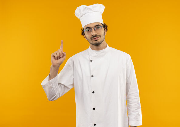 制服高兴的年轻男厨师穿着厨师制服 戴着眼镜点起来烹饪穿男