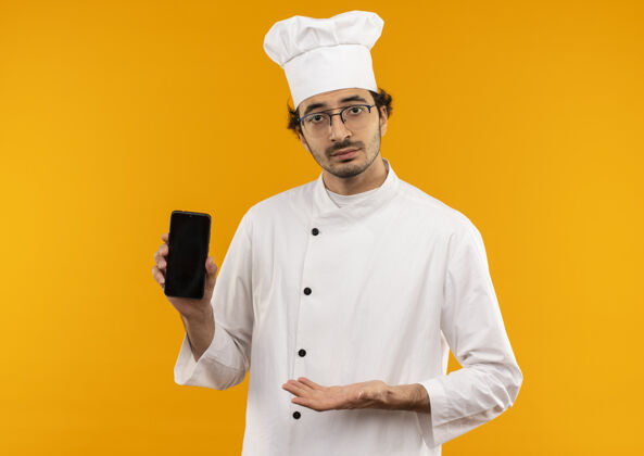 眼镜年轻的男厨师穿着厨师制服 戴着眼镜 手拿手指对着电话烹饪点制服