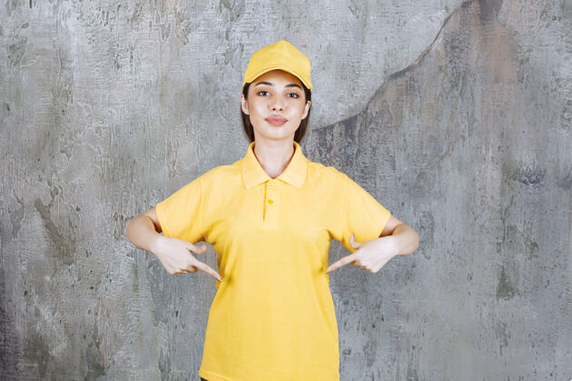 姿势身着黄色制服的女服务人员站在水泥墙上 展示自己地面聪明模特
