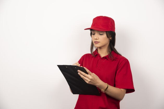纸板穿着红制服的年轻女送货员在白色背景的剪贴板上写字年轻人递送信使