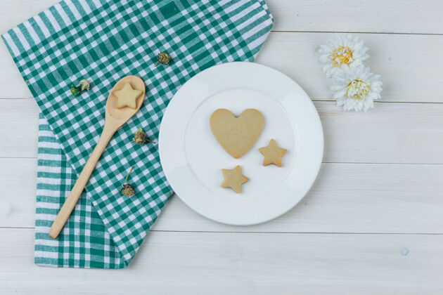 盘子一套鲜花和饼干放在盘子里 木勺放在木制和厨房毛巾的背景上平铺面包屑薯片糕点