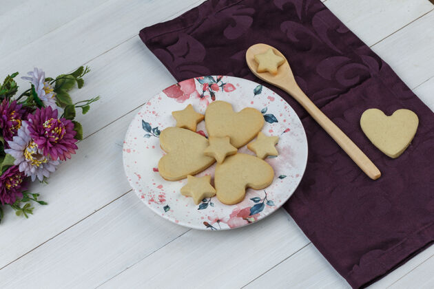 蛋糕盘子里的饼干和木制勺子 在木制和纺织品背景上有花的高角度视图木头脆花