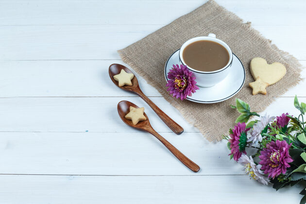 咖啡高角度看咖啡杯 心形和星形饼干放在一个带花的袋子上 饼干放在白色木板背景上的木勺里水平角度美味杯子